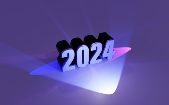 The image consists of the number 2024 in bold, three-dimensional text that seems to be illuminated by colorful lights. The background is a rich purple hue with blue and pink lighting effects casting shadows and reflections on the surface.