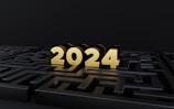 Golden numbers spelling out 2024 sit on top of a dark, intricate maze. The lighting highlights the numbers, creating a striking contrast with the black background.