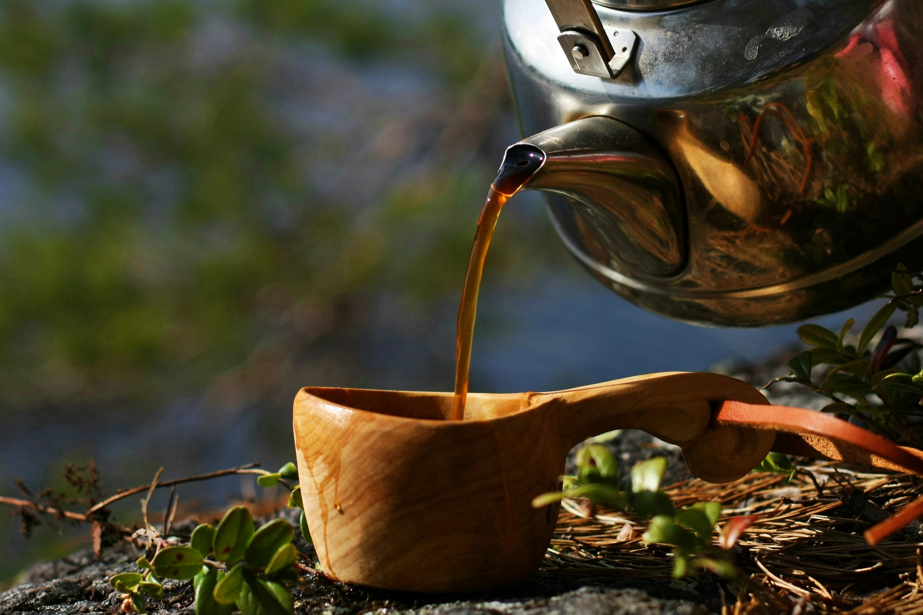 a tea kettle pouring tea into a wooden cup