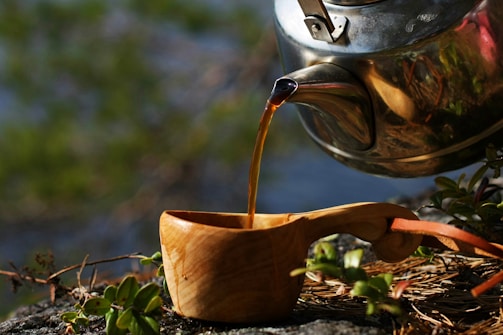 Artisanal herbalist hand-pouring freshly brewed arbutus tea into a ceramic cup.