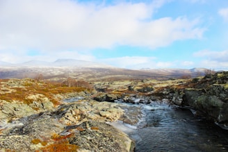 a stream running through a rocky landscape with mountains in the background