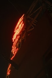A neon sign with vibrant red lighting against a dark background, mounted on a metal frame.