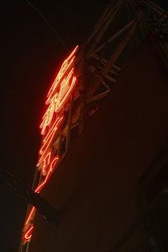 A neon sign with vibrant red lighting against a dark background, mounted on a metal frame.