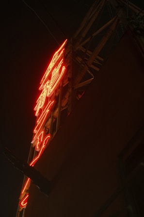 A neon sign with vibrant red lighting against a dark background, mounted on a metal frame.