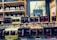 Bottles of various flavored liqueurs are displayed in rows, each labeled with distinct flavors such as Limoncello, Haselnuss, and Peche Rouge. The backdrop includes a shelf filled with additional bottles of spirits and a decorative sign featuring botanical illustrations.