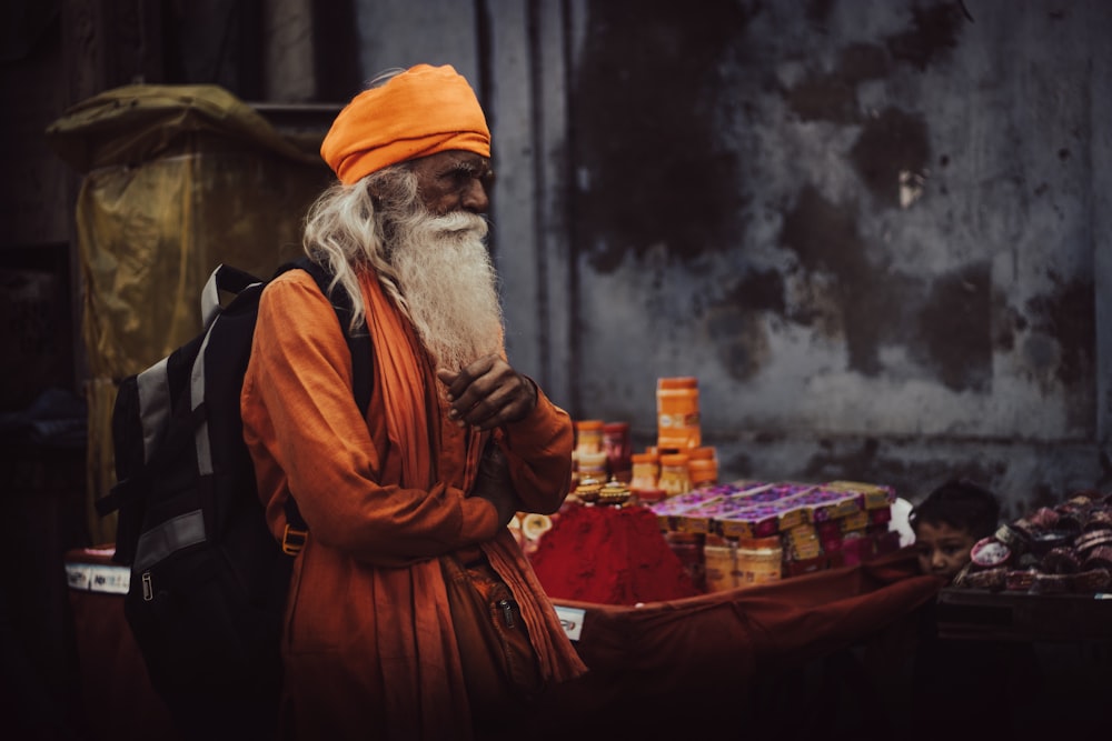 a man with a long white beard and orange turban stands in front of