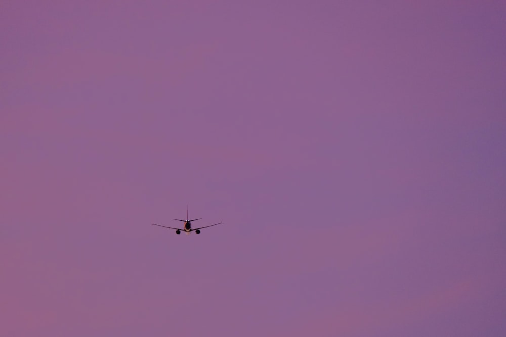 an airplane is flying in the purple sky