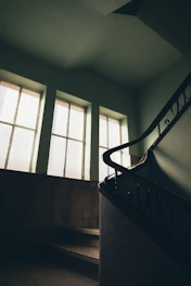A warm walnut staircase with sturdy handrails blending into a dark green painted wall.