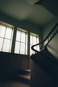 A warm walnut staircase with sturdy handrails blending into a dark green painted wall.