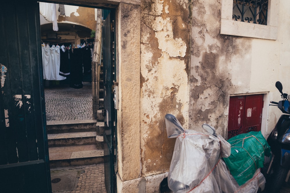 a scooter parked next to a building with a bag of garbage on the