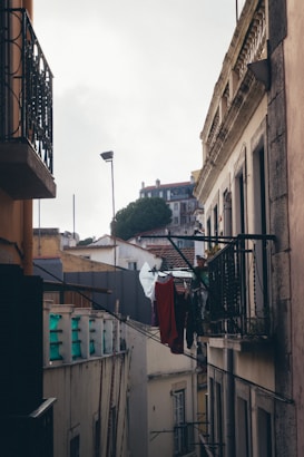 An urban alleyway with closely situated buildings and balconies. Clothes of various colors hang on a line between the buildings, suggesting a residential area. The scene conveys a sense of everyday life in a densely populated neighborhood.