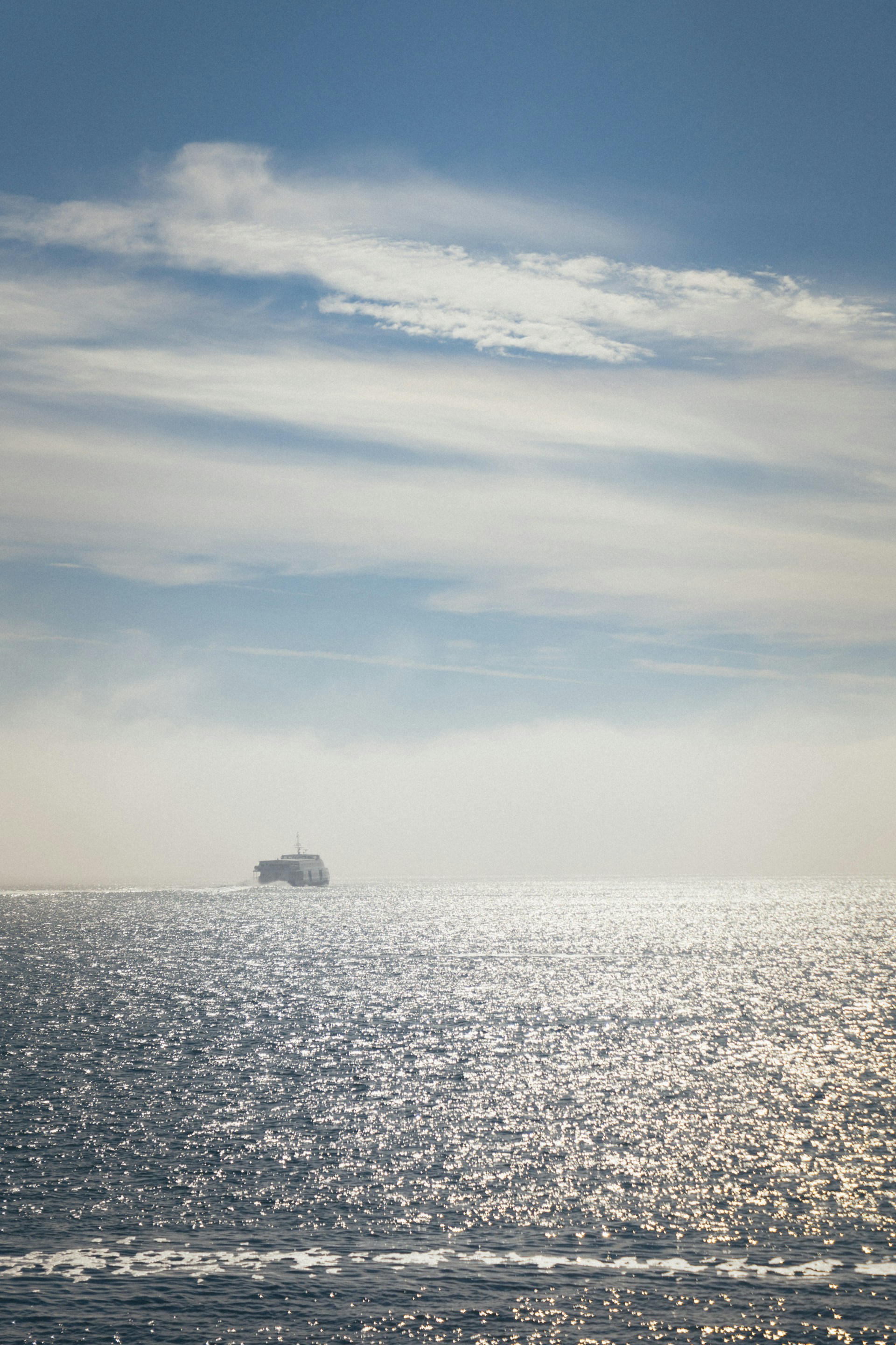 A scenic view of a vibrant blue sky reflecting on the calm sea, with a ferry sailing in the distance.