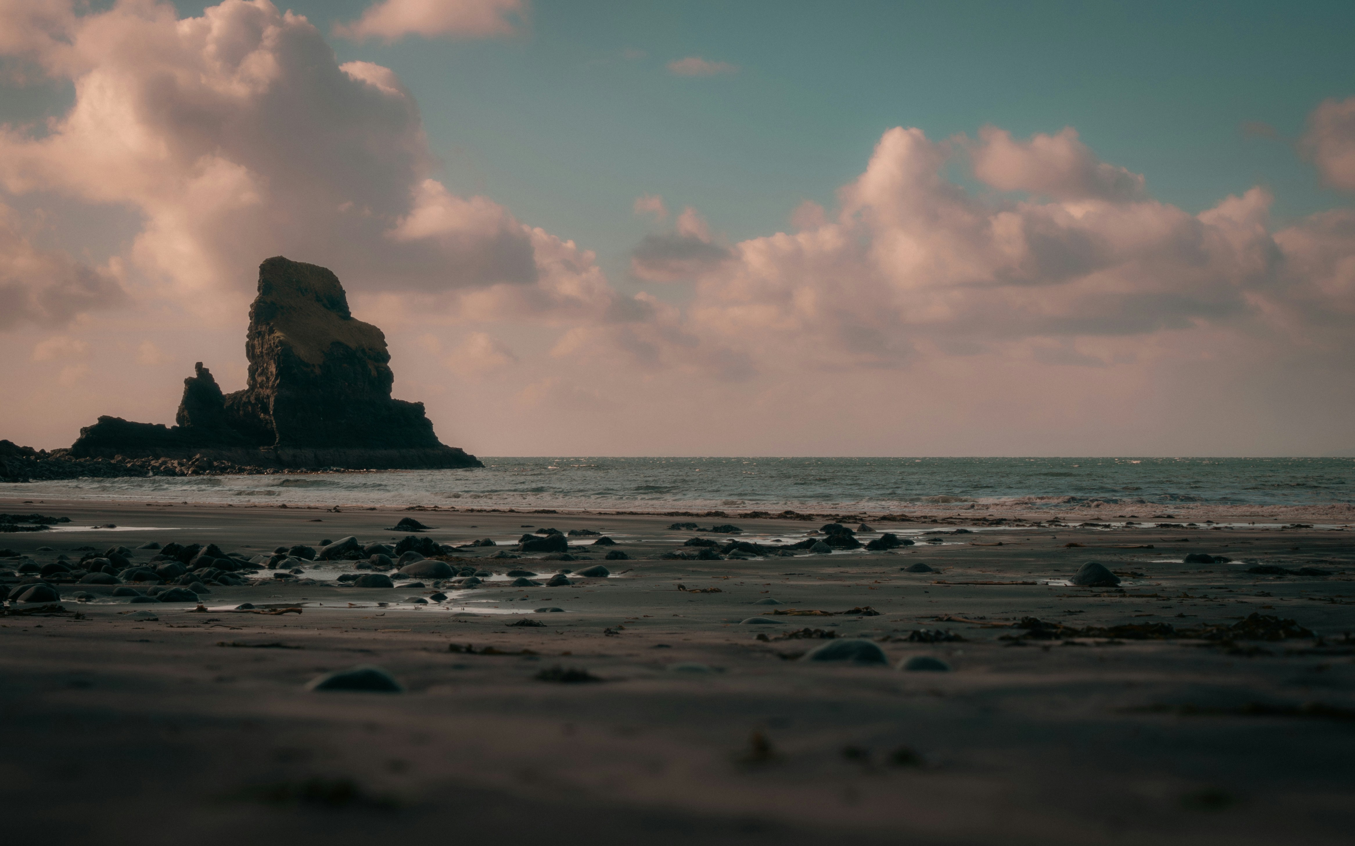 a beach with rocks and water under a cloudy sky, 