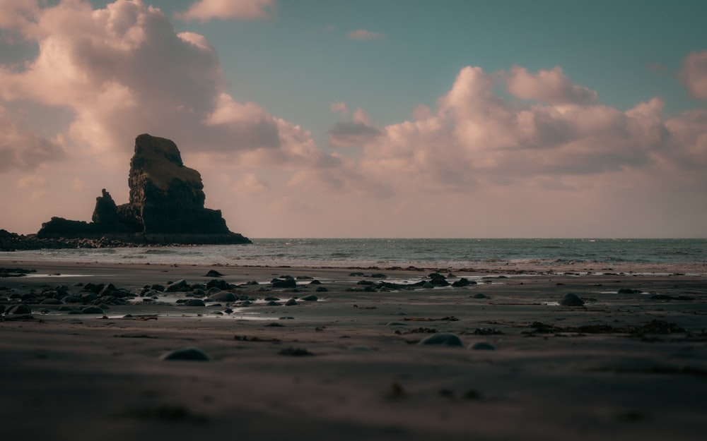 a beach with rocks and water under a cloudy sky