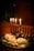 A silver menorah with lit candles in different colors sits on a wooden table, surrounded by freshly baked pastries sprinkled with powdered sugar, and small wooden spinning tops, called dreidels.