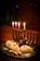 A silver menorah with lit candles in different colors sits on a wooden table, surrounded by freshly baked pastries sprinkled with powdered sugar, and small wooden spinning tops, called dreidels.