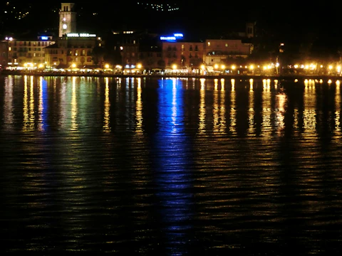 Night view of a waterfront building with neon reflections shimmering on the water.