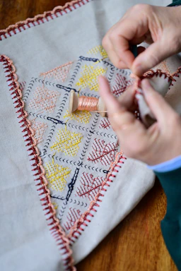 Close-up of hands delicately stitching a vibrant cherry blossom pattern on fabric.