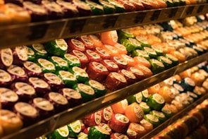 Shelves are filled with an array of colorful, packaged cheese wheels. The cheese wheels are neatly arranged and displayed under warm lighting, enhancing their vibrant colors like green, red, orange, and purple.