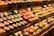 Shelves are filled with an array of colorful, packaged cheese wheels. The cheese wheels are neatly arranged and displayed under warm lighting, enhancing their vibrant colors like green, red, orange, and purple.