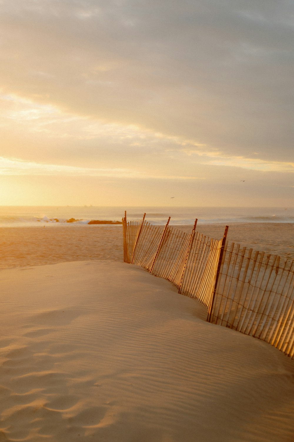 a sandy beach with a fence and ocean in the background
