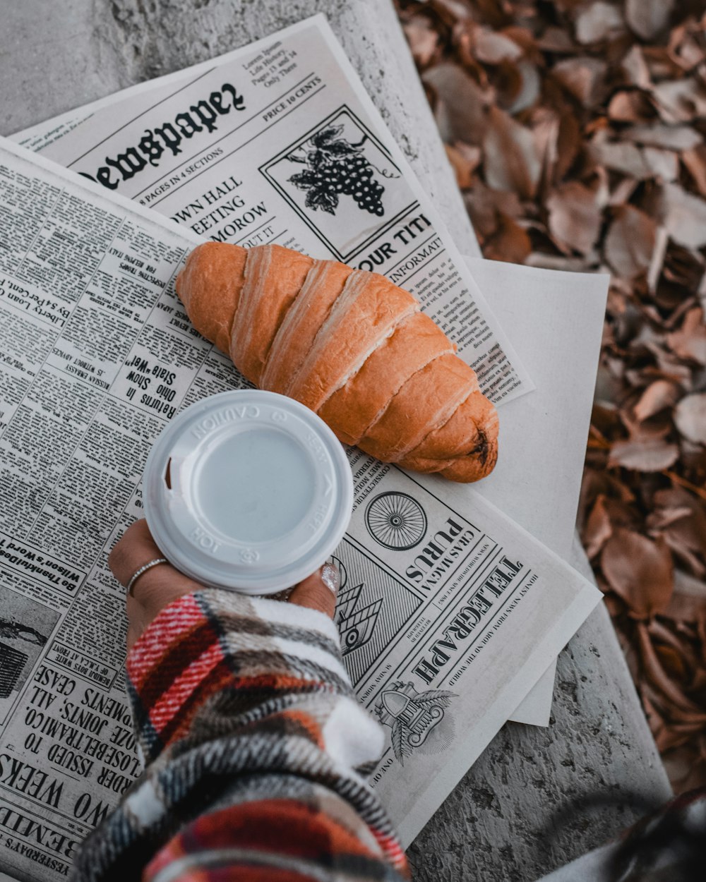 a person holding a coffee cup next to a croissant