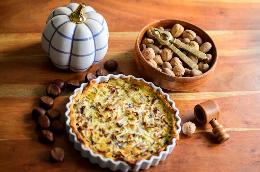 a pie sitting on top of a wooden table next to a bowl of nuts