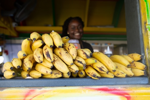 A friendly customer service representative holding a bunch of ripe bananas with a warm smile.