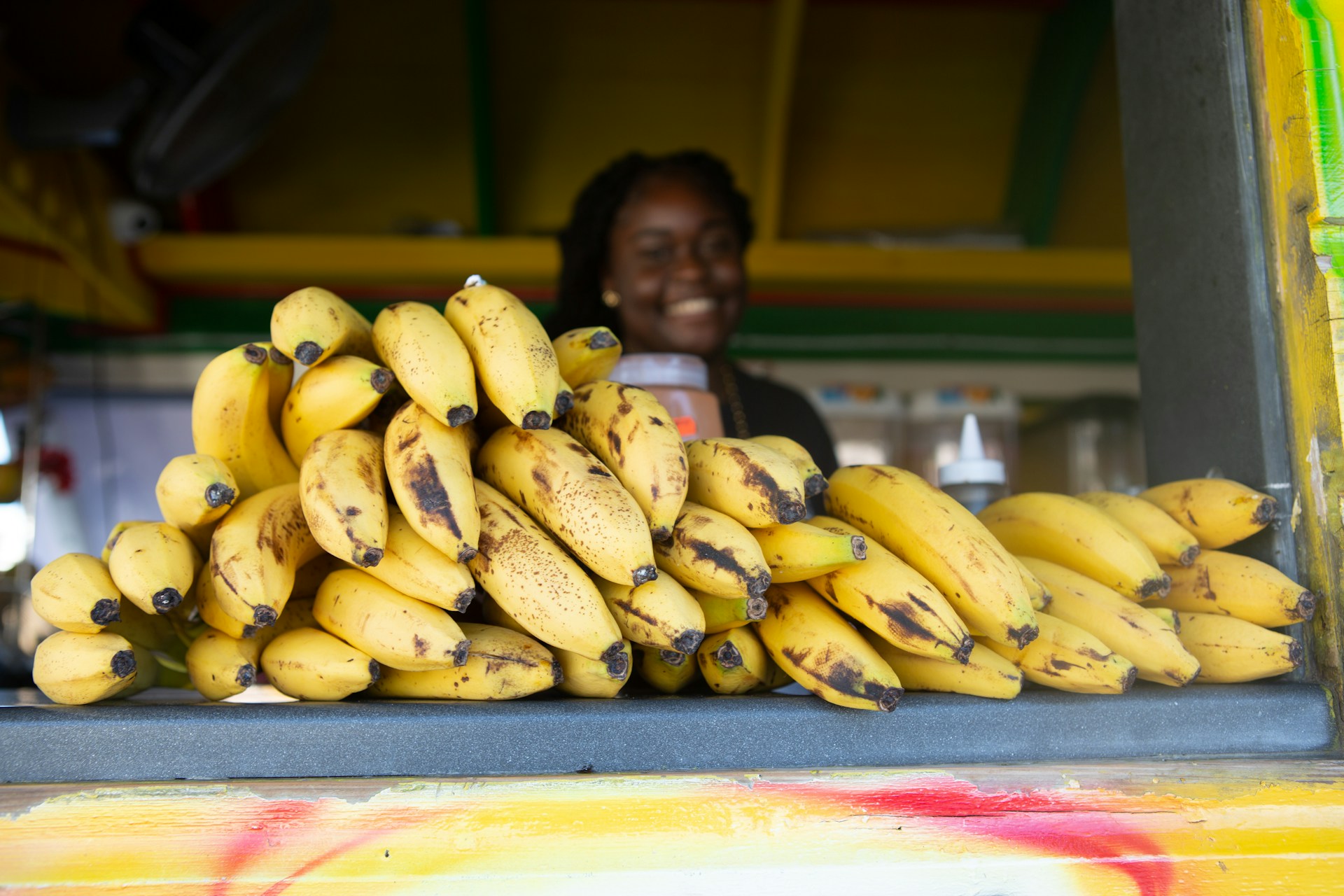 a woman standing behind a pile of ripe bananas