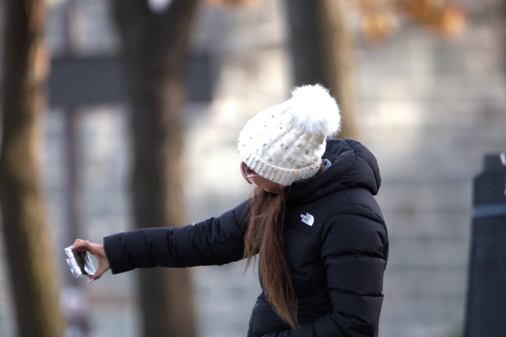 a woman in a black jacket and a white hat holding a cell phone