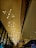 An elegant and spacious interior features a high ceiling adorned with modern, geometric chandeliers composed of multiple glowing bulbs. The design elements include a combination of linear and curvilinear structures with warm lights reflecting off glass and metal surfaces.