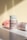 Two bottles of MultiFirst advanced formula adult multivitamins are displayed on a flat surface. The bottle in the foreground stands upright with legible text describing its benefits. The second bottle lies on its side, partially visible. A pink rose lies in the background, adding a soft touch to the composition. The lighting creates soft shadows and highlights on the surfaces.
