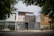 A modern urban house exterior with a clean and minimalistic design. The facade features geometric patterns with a combination of white and gray colors. Large windows and a metal gate add to the contemporary aesthetic. Surrounding the house are green leafy trees, providing a natural contrast.
