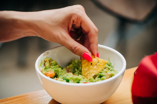 Hand dipping a tortilla chip into a bowl of fresh guacamole