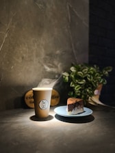A cozy coffee cup with steam rising, placed on a wooden table next to a slice of carrot cake.