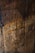 A close-up view of a weathered wooden surface with visible grain patterns and carved initials. The wood exhibits a rustic and aged texture, with various shades of brown and some visible nail holes.