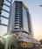 A tall and modern office building with a glass facade, featuring multiple balconies and a distinctive angled roof. It is situated in an urban area with some cars parked outside and a few people walking nearby. The structure appears sleek and well-maintained, with a sign reading 'MAPUTO BUSINESS TOWER' at the entrance.