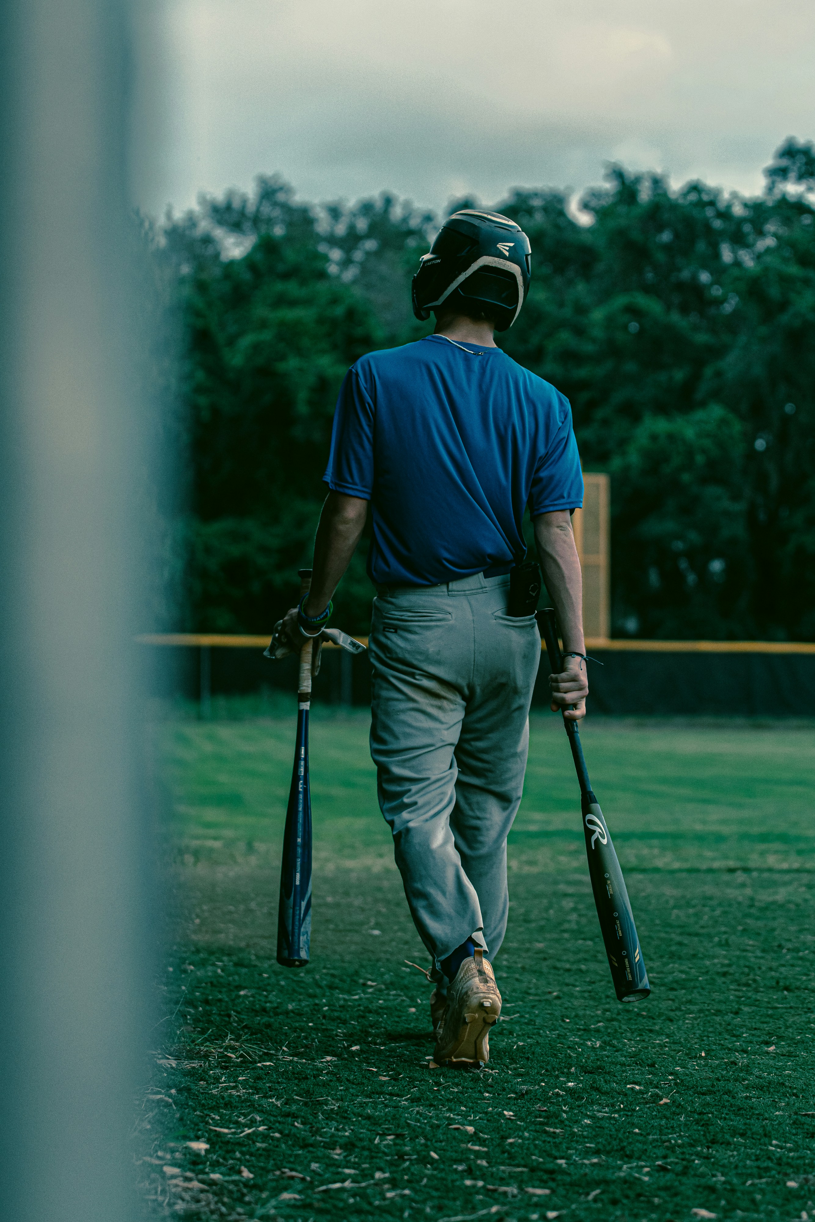 a man walking across a field holding two baseball bats