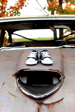 Close-up of a colorful clown shoe resting on a classic car hood.