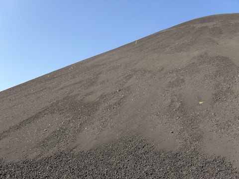 A steep slope covered in dark, fine volcanic ash under a clear blue sky.