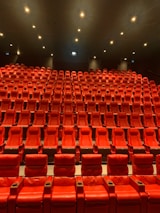 A large, empty movie theater with rows of red recliner seats arranged in a gradient pattern facing the front. Soft ambient lighting casts a warm glow, creating a cozy atmosphere.