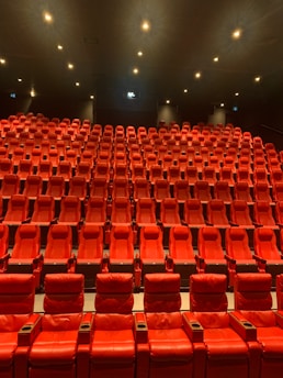 A large, empty movie theater with rows of red recliner seats arranged in a gradient pattern facing the front. Soft ambient lighting casts a warm glow, creating a cozy atmosphere.