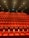 A large, empty movie theater with rows of red recliner seats arranged in a gradient pattern facing the front. Soft ambient lighting casts a warm glow, creating a cozy atmosphere.