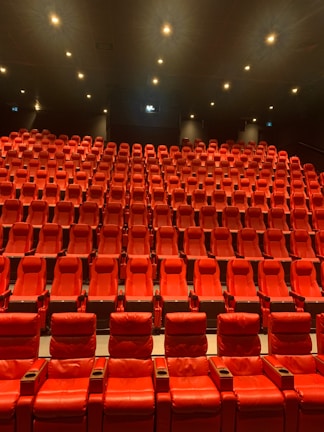 A large, empty movie theater with rows of red recliner seats arranged in a gradient pattern facing the front. Soft ambient lighting casts a warm glow, creating a cozy atmosphere.