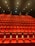 A large, empty movie theater with rows of red recliner seats arranged in a gradient pattern facing the front. Soft ambient lighting casts a warm glow, creating a cozy atmosphere.