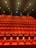 A large, empty movie theater with rows of red recliner seats arranged in a gradient pattern facing the front. Soft ambient lighting casts a warm glow, creating a cozy atmosphere.