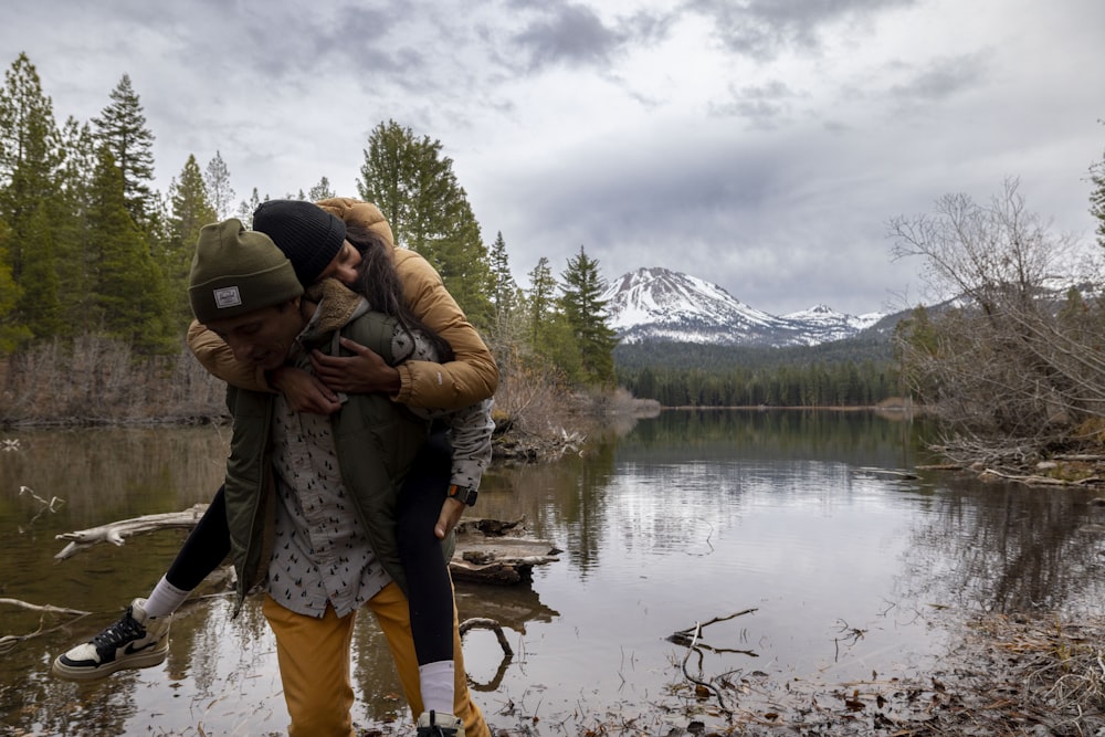 a man holding a woman in his arms near a lake