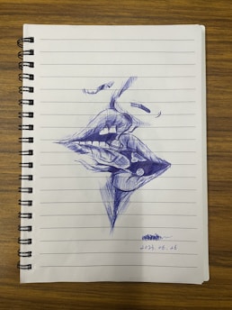 A ballpoint pen drawing on a lined notebook page depicts abstract, surrealistic intertwined lips and facial features. The drawing is detailed with cross-hatching and shading, suggesting depth and texture.