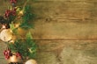 A rustic wooden surface adorned with festive decorations on the side, including pine branches, red berries, pinecones, and glowing lights, creating a seasonal and natural atmosphere.
