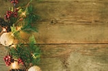 A rustic wooden surface adorned with festive decorations on the side, including pine branches, red berries, pinecones, and glowing lights, creating a seasonal and natural atmosphere.